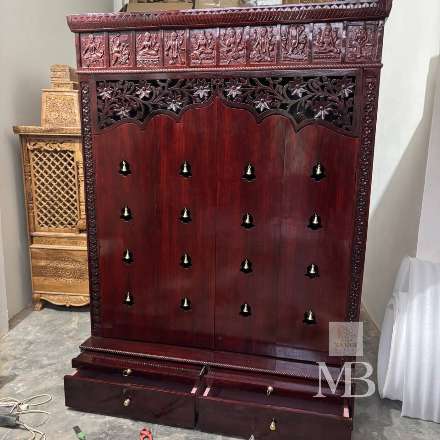 Dark brown wooden pooja mandir with carved floral panels, brass bell accents and spacious storage drawers