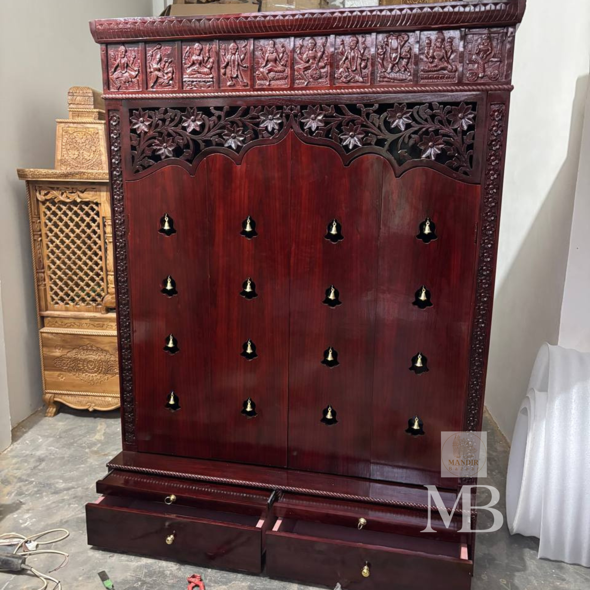 Dark brown wooden pooja mandir with carved floral panels, brass bell accents and spacious storage drawers