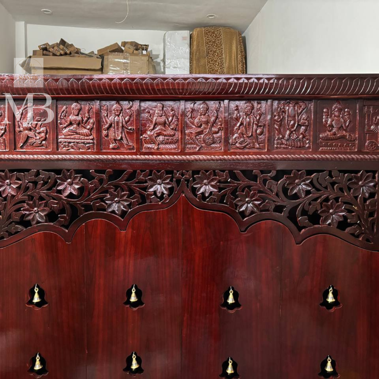 Dark brown wooden pooja mandir with carved floral doors, brass bell details and storage drawers
