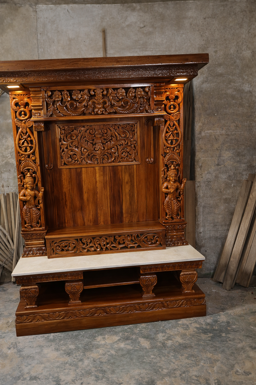 Hand carved wooden pooja mandir with intricate floral carvings, deity figures, marble-look platform and warm LED lights