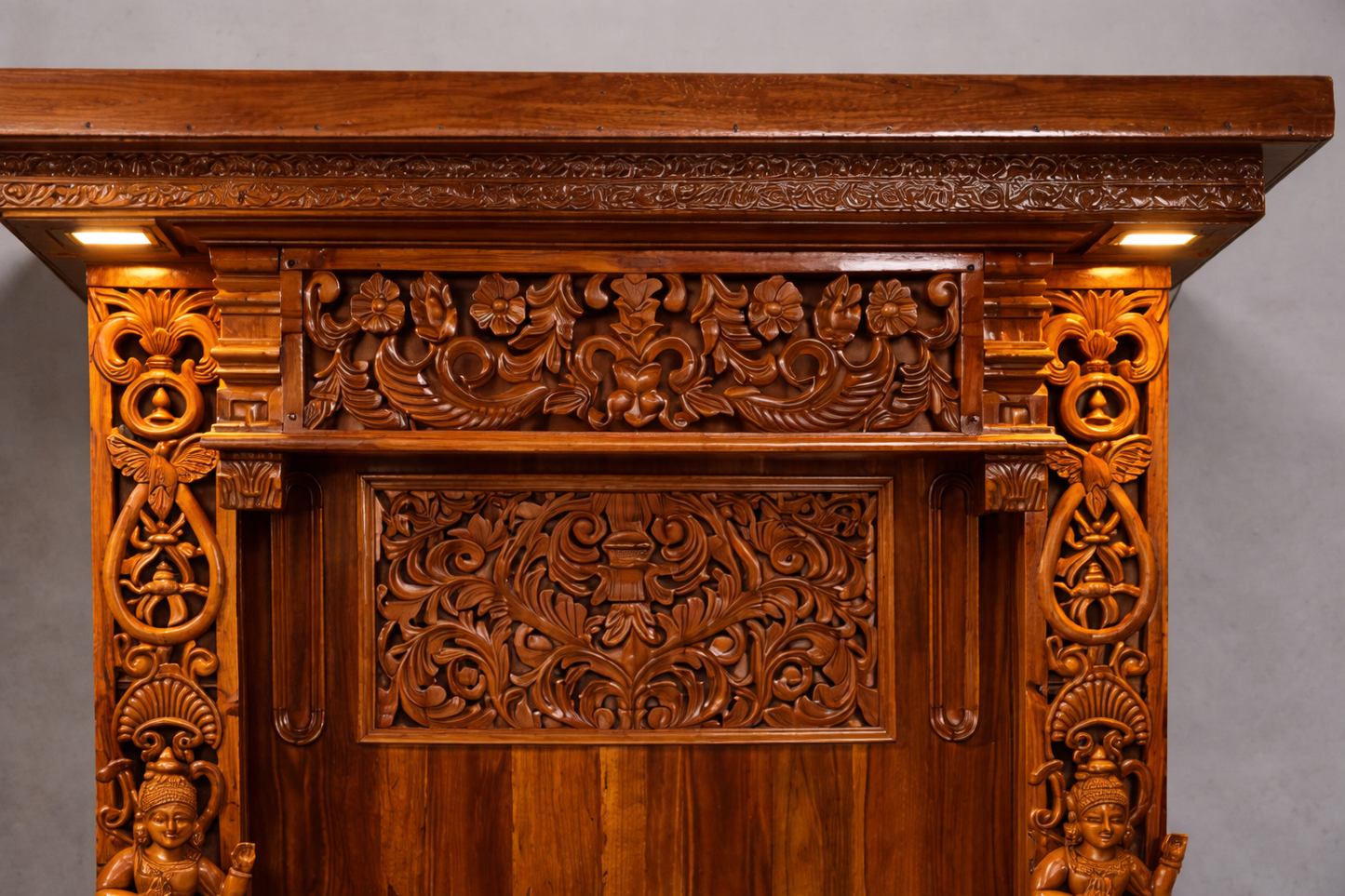 Hand carved wooden pooja mandir with intricate floral carvings, deity figures, marble-look platform and warm LED lights