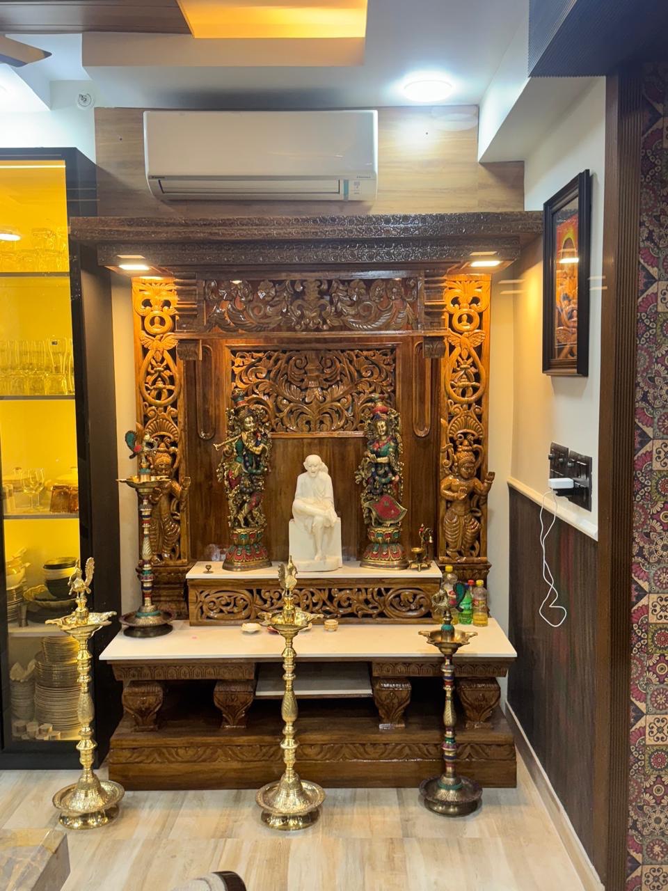Hand carved wooden pooja mandir with intricate floral carvings, deity figures, marble-look platform and warm LED lights