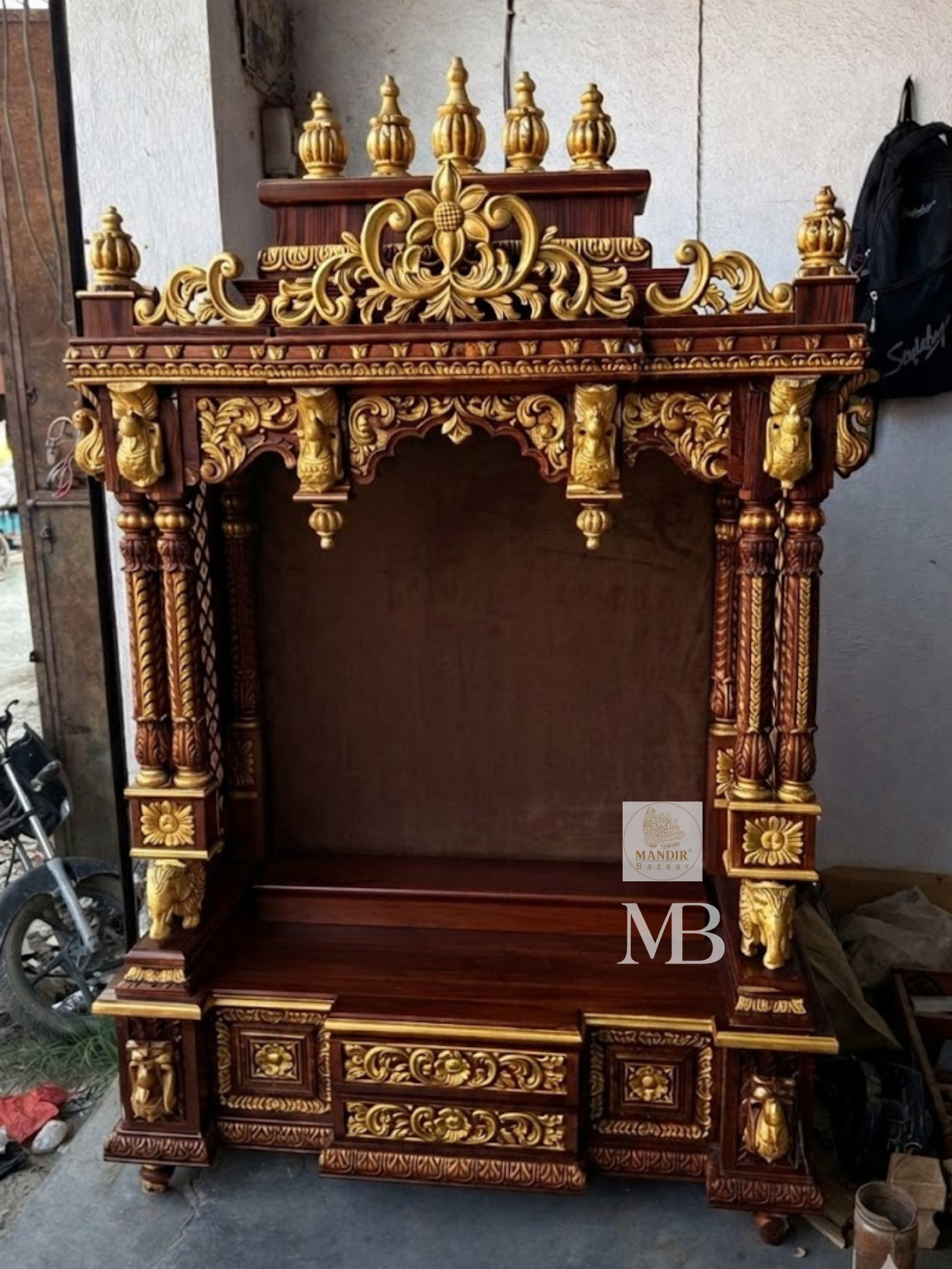 Detailed close up of golden kalash finials and hand-carved floral arch crown on dark wood temple