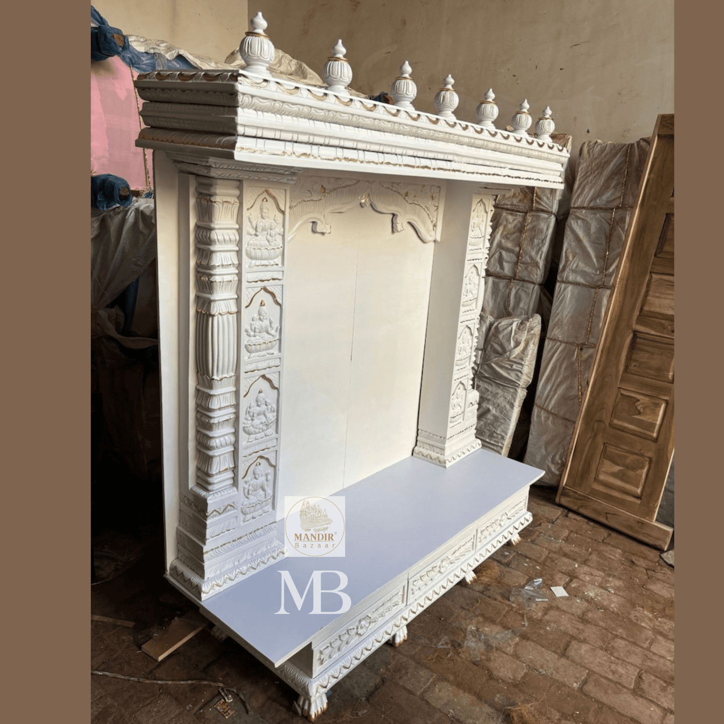 Three quarter view of white handcrafted wooden pooja temple showing base drawers and carved crown