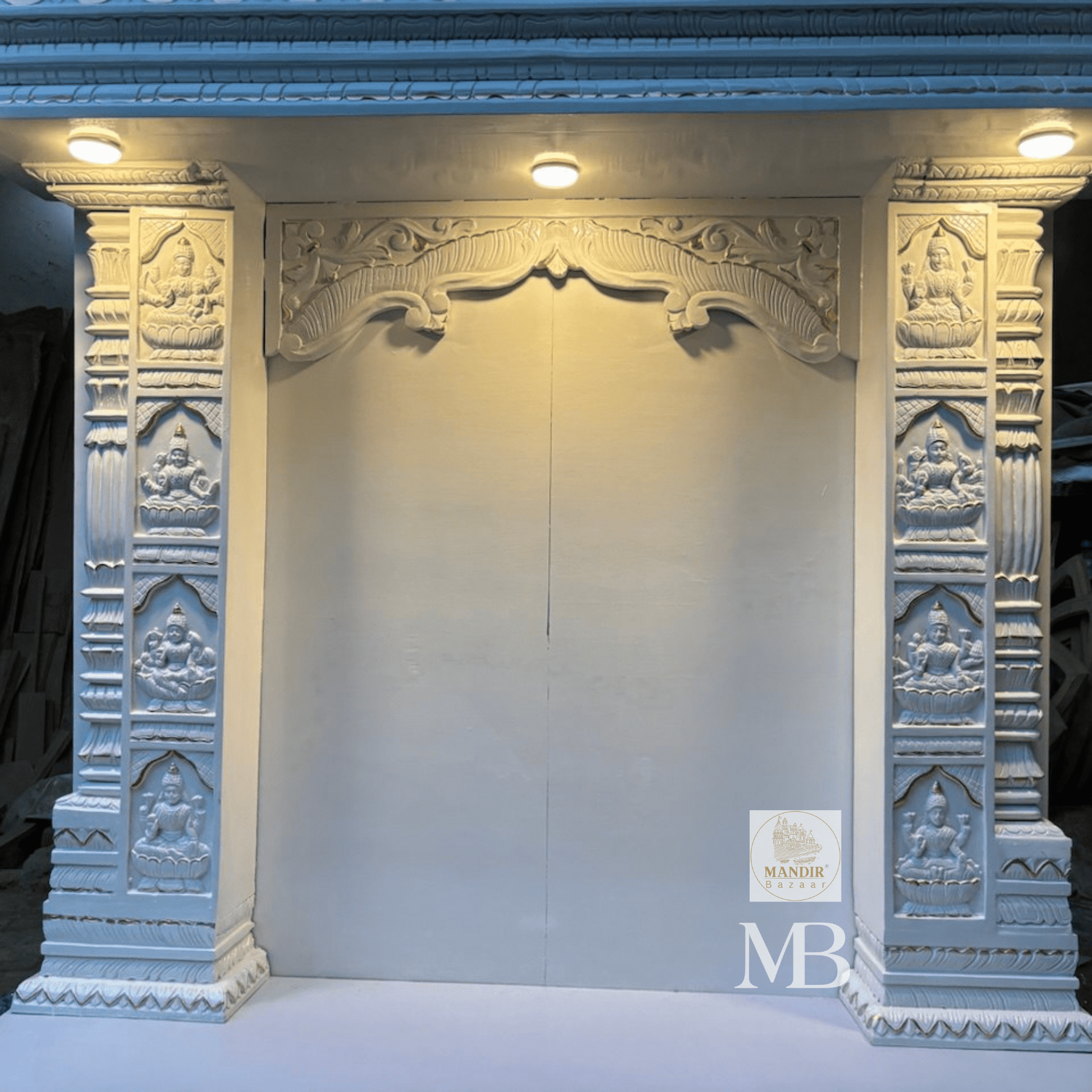 Close up view of hand-carved Goddess Lakshmi relief panels on front pillars of white wooden mandir