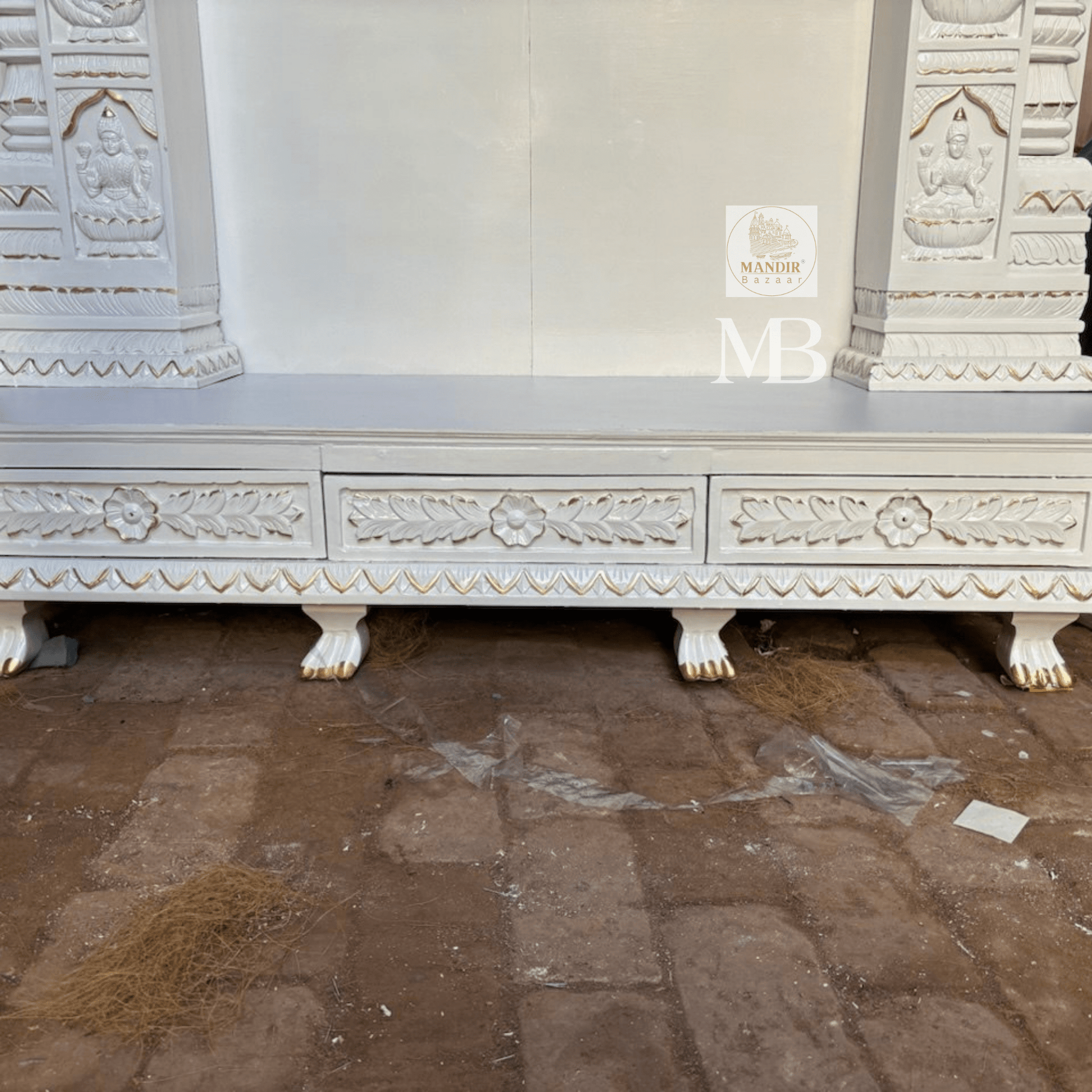 : Three quarter view of white handcrafted wooden pooja temple showing base drawers and carved crown