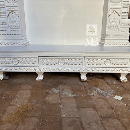 : Three quarter view of white handcrafted wooden pooja temple showing base drawers and carved crown