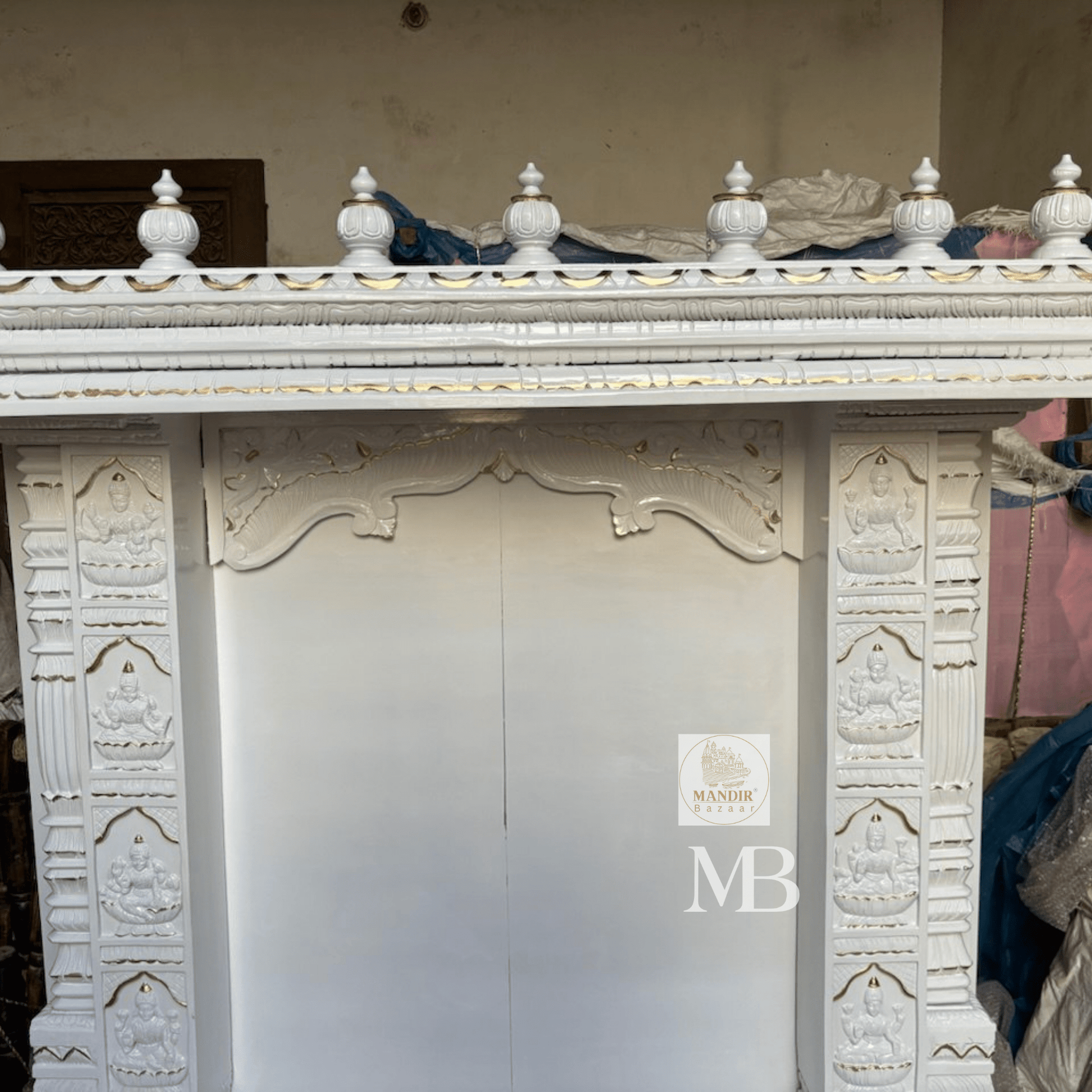 Close up view of hand-carved Goddess Lakshmi relief panels on front pillars of white wooden mandir